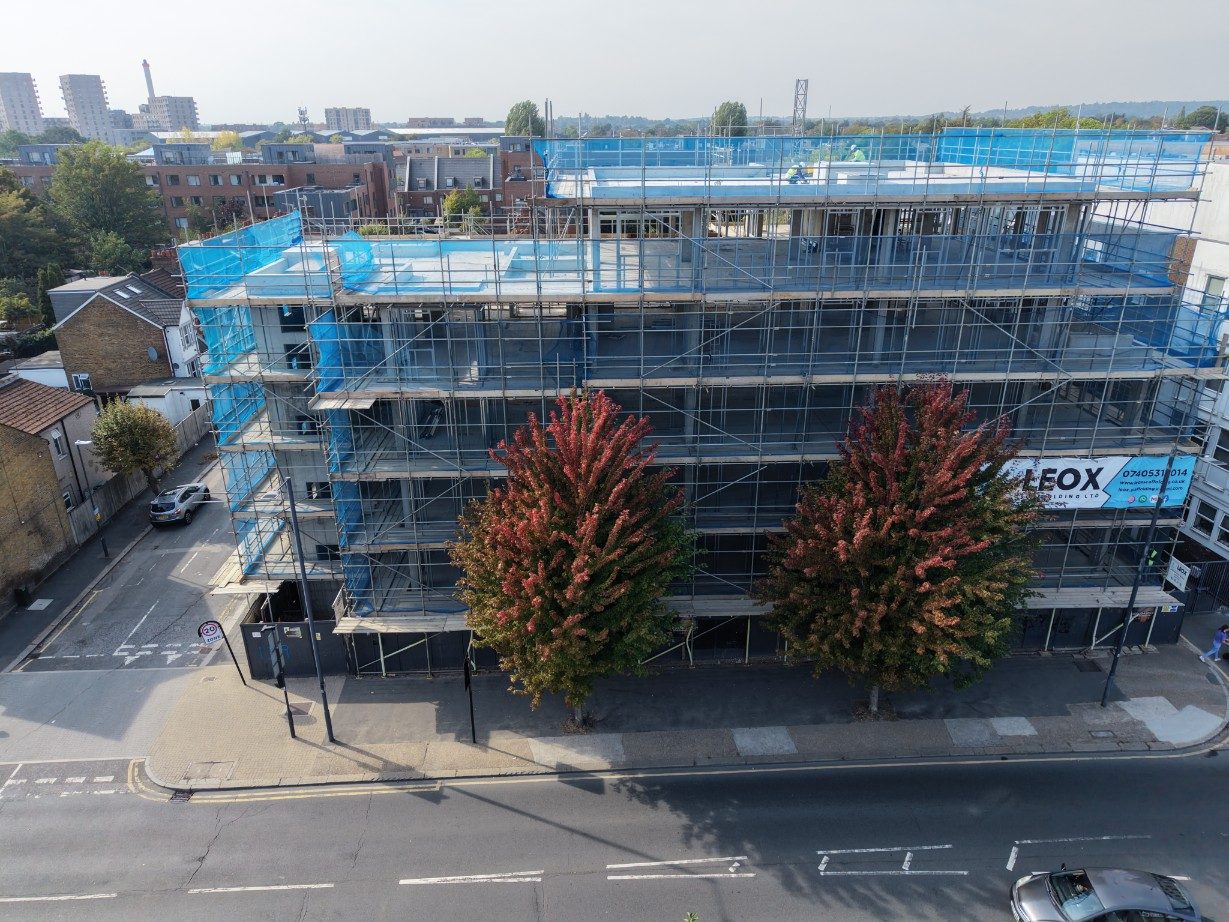 Street elevation of the development behind scaffold, with the top floor being framed under blue sheeting
